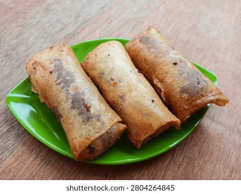A close-up shot of crispy fried spring rolls (lumpia) filled with sweet purple yam and melted chocolate. Served on a plate, highlighting the unique and delicious fusion of traditional Indonesian snack with modern sweet filling, perfect for food blogs and culinary content