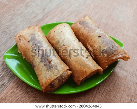 A close-up shot of crispy fried spring rolls (lumpia) filled with sweet purple yam and melted chocolate. Served on a plate, highlighting the unique and delicious fusion of traditional Indonesian snack with modern sweet filling, perfect for food blogs and culinary content