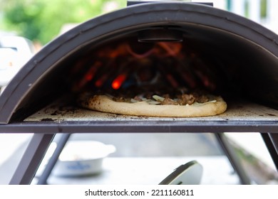 A Closeup Shot Of A Crusty Pizza Cooking In An Outdoors Oven In A Garden