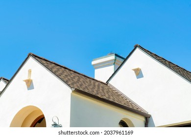 A closeup shot of dark open gable roofs of white buildings and a chimney under the blue sky