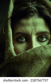 Close-up Shot Of A Dark-haired Girl, Wrapping Her Head And Face In Burlap Fabric And Looking Sadly At The Camera. Human Suffering, War. 