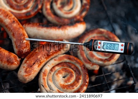 Close-up shot of a digital meat thermometer displaying a safe cooking temperature for grilled sausages