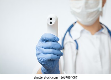 Nahaufnahme eines Arztes, der eine chirurgische Schutzmaske trägt, die bereit ist, das Infrarot-Stirn-Thermometer (Thermometer-Pistole) zu verwenden, um die Körpertemperatur auf Virussymptome zu überprüfen - Epidemic-Virus-Ausbruch-Konzept