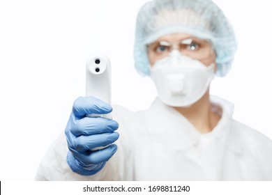 Close-up shot of doctor wearing protective suit abd surgical mask using infrared forehead thermometer (thermometer gun) to check body temperature for virus symptoms - coronavirus outbreak concept