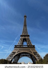 A close-up shot of the Eiffel Tower, capturing its intricate iron latticework against a clear sky. The image highlights the tower's architectural details, showcasing the iconic Parisian structure in s
