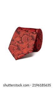 Close-up shot of an elegant red and black tie embossed with a floral paisley pattern. The paisley red and black tie is rolled and isolated on a white background. Top view.