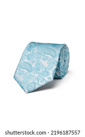 Close-up shot of an elegant turquoise and white tie embossed with a floral paisley pattern. The paisley turquoise and white tie is rolled and isolated on a white background. Top view.