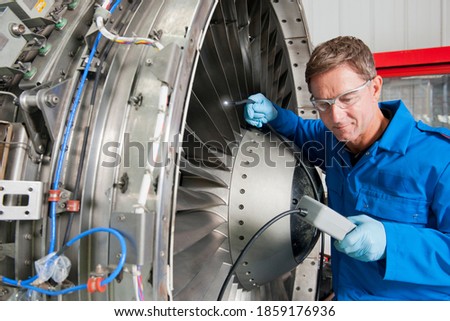 Close-up shot of an engineer inspecting the turbine engine of a passenger jet at a hangar.