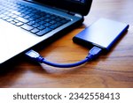 A closeup shot of an external HDD connected to a laptop on a wooden table