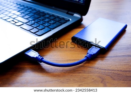 A closeup shot of an external HDD connected to a laptop on a wooden table