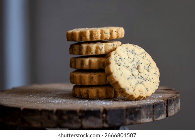 A close-up shot features a stack of golden-brown shortbread cookies, speckled with poppy seeds. They rest on a rustic wooden surface dusted with powdered sugar.