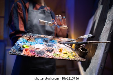 Close-up Shot of Female Artist Hand, Holding Paint Brushes and Palette. Colorful, Oil Painting in the background. - Shutterstock ID 1866213736