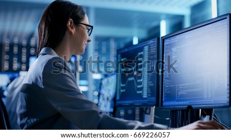 Close-up Shot of Female IT Engineer Working in Monitoring Room. She Works with Multiple Displays.