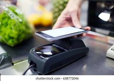 Closeup Shot Of Female Hand Holding Smartphone Over Terminal Using NFC Payment Technology In Grocery Store