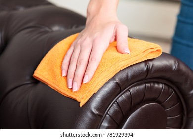 Closeup shot of female hand wiping brown leather chester couch of sofa