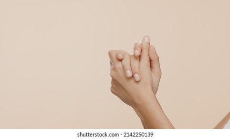 Close-up shot of female hands are rubbed and interlocked on beige background | Hand care commercial concept