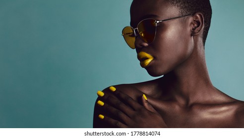 Close-up shot of female model bright makeup and sunglasses on grey background. Attractive african woman with buzzcut posing in studio.
