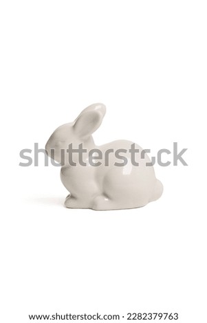 Close-up shot of a figure of a white ceramic bunny, covered with glossy glaze. The statuette is isolated on a white background. Side view.