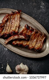 Closeup Shot Of Flavorful Grilled Pork Ribs In Thick Barbeque Sauce Cut In Messy Way Served In Vintage Metal Tray On Dark Textured Background. Pub Styling Concept.