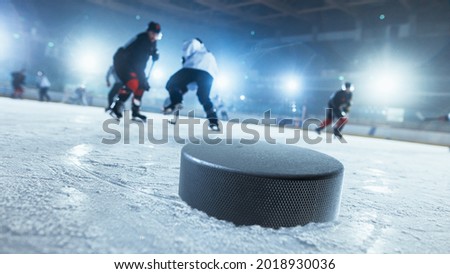 Close-up Shot with Focus on a 3D Hockey Puck on Ice Hockey Rink Arena. In the Background Blurred Professional Players From Different Teams Trying to Get the Puck. Dutch Angle Shot.