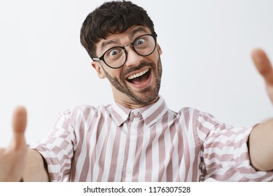 Close-up Shot Of Funny Emotive And Happy Good-looking Modern Male Hipster In Glasses And Pink Striped Shirt Pulling Hands Towards Camera To Make Selfie, Aping And Making Faces, Fooling Around