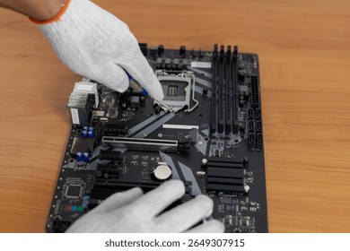  A close-up shot of gloved hands using a tool to work on the CPU (Central Processing Unit) socket area of a black computer motherboard.