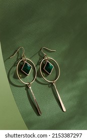 Close-up shot of gold earrings with pendants. The earrings are decorated with two gold pendants and a green square pendant. The earrings are isolated on a green background. Top view.