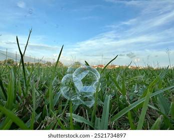 A close-up shot of green grass with a bubble or transparent orb reflecting the sky. The image has a serene and playful feel.