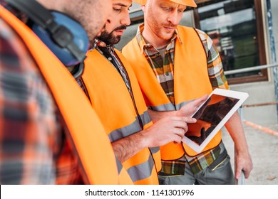 Close-up Shot Of Group Of Builders Using Digital Tablet At Construction Site