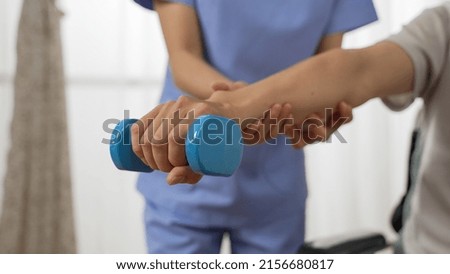closeup shot hand of disabled person going through rehab training using a dumbbell. cropped female nursing aide provided assistance at background