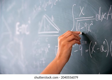 Close-up shot of a hand holding chalk and writing mathematical equations on the blackboard. Education concept.