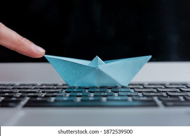 A Closeup Shot Of A Hand Holding A Paper Boat On Top Of A Laptop