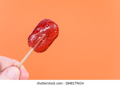 Nahaufnahme einer Hand mit rotem Lollipop einzeln auf orangefarbenem Hintergrund
