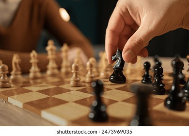 Close-up shot of a hand moving a black chess piece during a game between two players. The focus is on the chessboard and pieces, capturing the strategic nature of the game