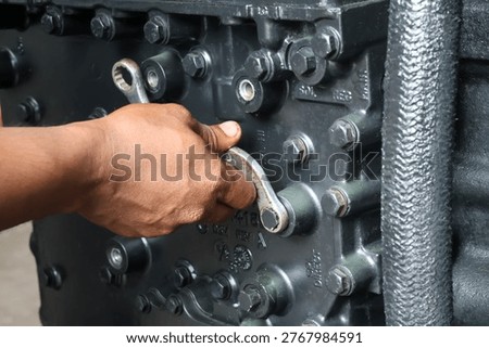 ​A close-up shot of a hand using an offset ring spanner to secure a bolt on a heavy-duty industrial engine component during a repair.