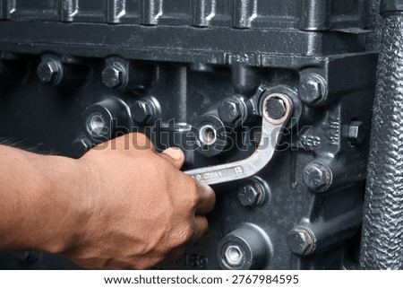 ​A close-up shot of a hand using an offset ring spanner to secure a bolt on a heavy-duty industrial engine component during a repair.