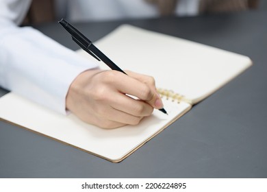 Closeup Shot Of Hand Young Student Lady Freelancer Journalist Writing Article Using Copybook In Gray Modern Home Office. Remote Job, Education And Career Profession Concept. Copy Space