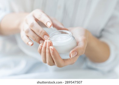 Closeup shot of hands applying moisturizer. Beauty woman holding a glass jar of skin cream. Shallow depth of field with focus on moisturizer. - Shutterstock ID 289547507