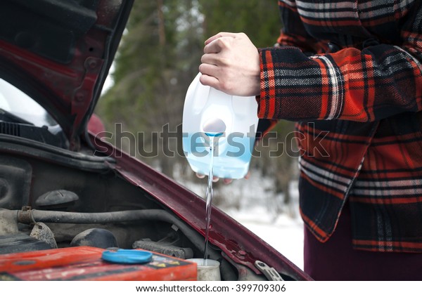 Closeup shot of hands holding bottle with antifreeze\
washer fluid and pouring it into windshield washer tank in winter\
day.