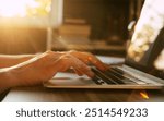 A close-up shot of hands typing on a laptop keyboard, bathed in warm sunlight. The soft glow and gentle lighting create a serene and productive atmosphere, ideal for focused work or creative tasks.