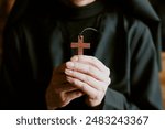 Closeup shot of hands of unrecognizable mature Catholic nun wearing black habit holding wooden cross