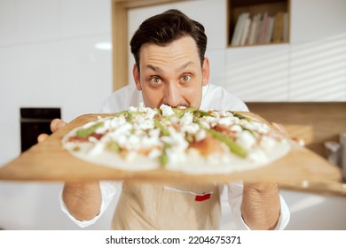 Close-up shot handsome chef man showing self made pizza for camera. Homemade pizza with asparagus feta salami mushrooms on wooden tray before putting in oven. - Powered by Shutterstock