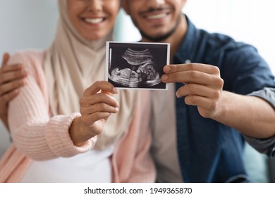 Closeup shot of happy pregnant muslim couple demonstrating baby sonography photo while relaxing together at home, showing first photo of their child, enjoying future parenthood, cropped image - Shutterstock ID 1949365870