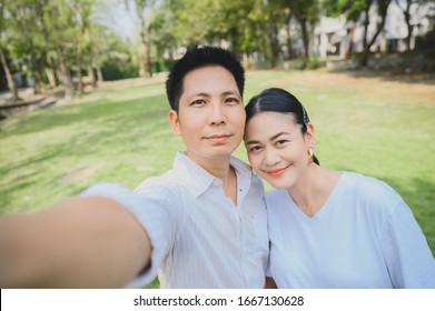 Closeup shot of Happy smiling Asian couple take selfie outdoor. A man taking a photo with his wife in the park - Powered by Shutterstock