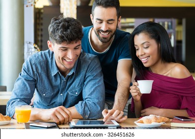 Closeup shot of happy young friends using digitaltablet during breakfast. Smiling men and woman doing breakfast at coffee bar. Happy young friends looking at palmtop and having a joyful breakfast.

