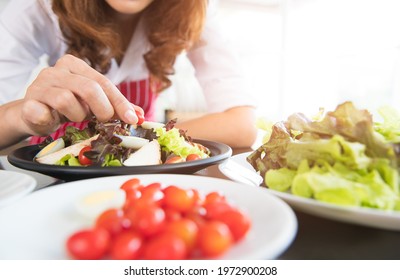 Closeup Shot Of Houswife Hand Decorating Chicken Breast Green Mixed Vegetable Salad With Boiled Egg Yolk On Countertop Desk In Kitchen With Raw Fresh Organic Material In Blurred Foreground.