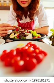 Closeup Shot Of Houswife Hand Decorating Chicken Breast Green Mixed Vegetable Salad With Boiled Egg Yolk On Countertop Desk In Kitchen With Raw Fresh Organic Material In Blurred Foreground.