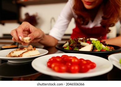 Closeup Shot Of Houswife Hand Decorating Chicken Breast Green  Vegetable Salad With Boiled Egg Yolk On Countertop Desk In Kitchen With Raw Fresh Organic Material In Blurred Foreground.