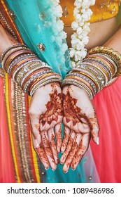 The close-up shot of Indian bride with beautiful saree in yellow blouse and red legenha showing hand with mehndi painted (henna) with a lot of glitter bracelets (bangle) on her wrist