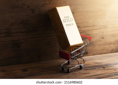 Closeup Shot Of A Large Shiny Gold Bar Put In A Tiny Shopping Cart With Wooden Wall Background.